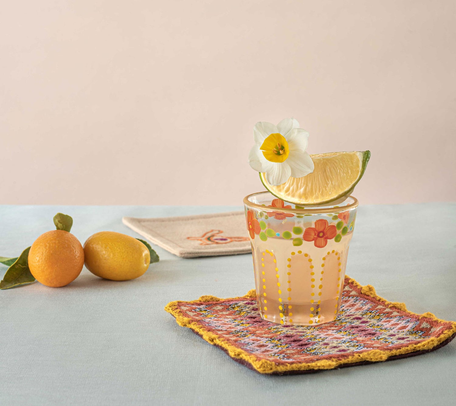 A shot glass with hand-painting on top of hand embroidered coaster