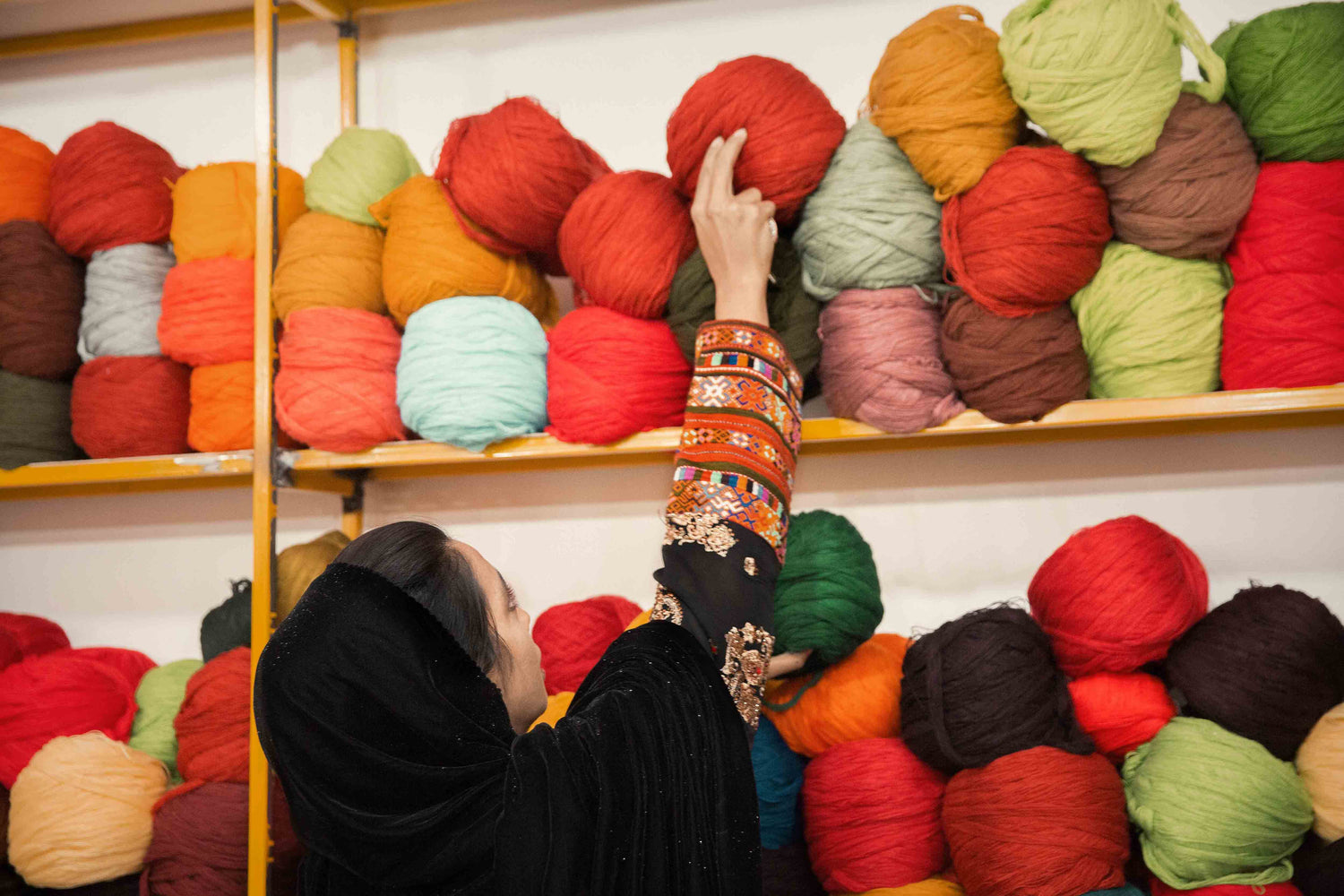 a woman picking colorful yarns from a shelf