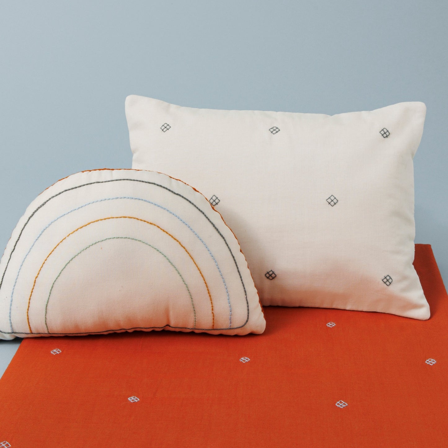Embroidered baby bedding set including an ivory rainbow decorative cushion, an ivory pillow and a paprika blanket