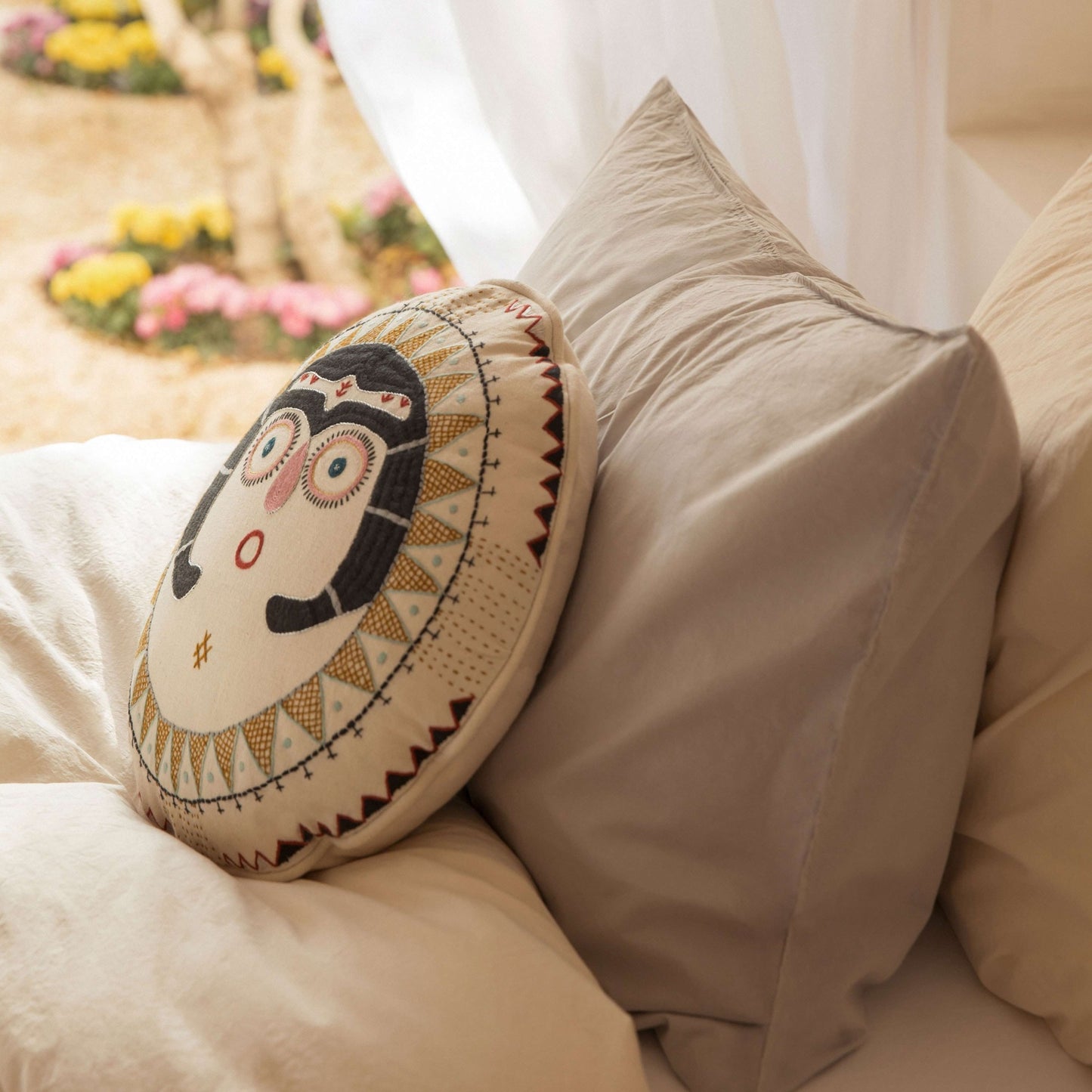 charcoal Sun Lady cushion on a bed next to grey and beige bedlinen