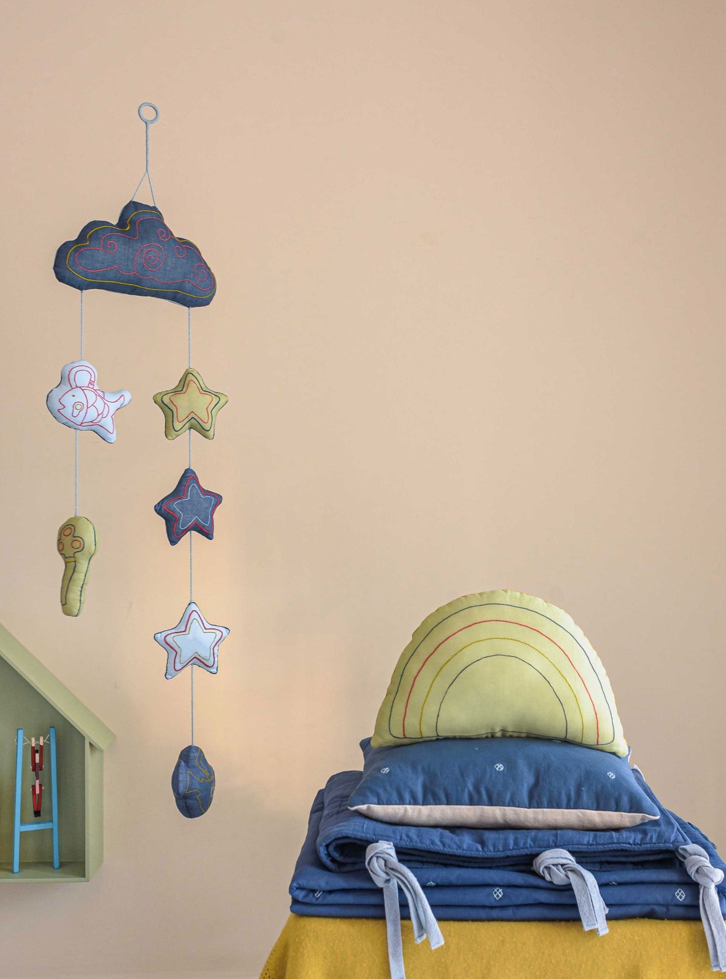 Blue bandook pillow, blanket, bumper with Lime rainbow decorative cushion stacked on top of each other while blue Moshkel gosha mobile is hanging from the ceiling