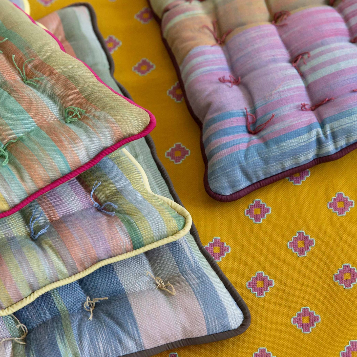 All colors of Royal Road square seat pad placed on a mustard Apadana table runner