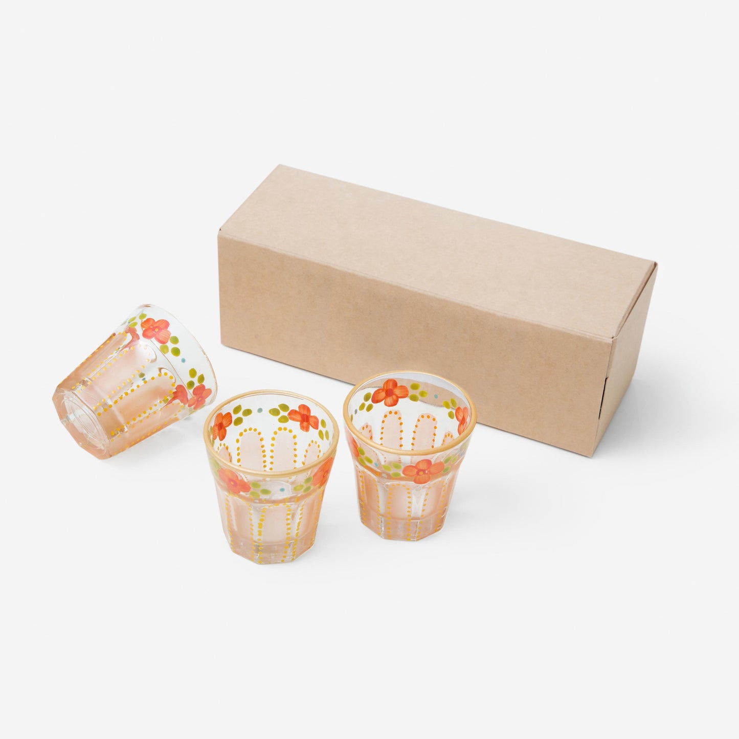 Three coral Saghi shot glasses next to a kraft packaging box