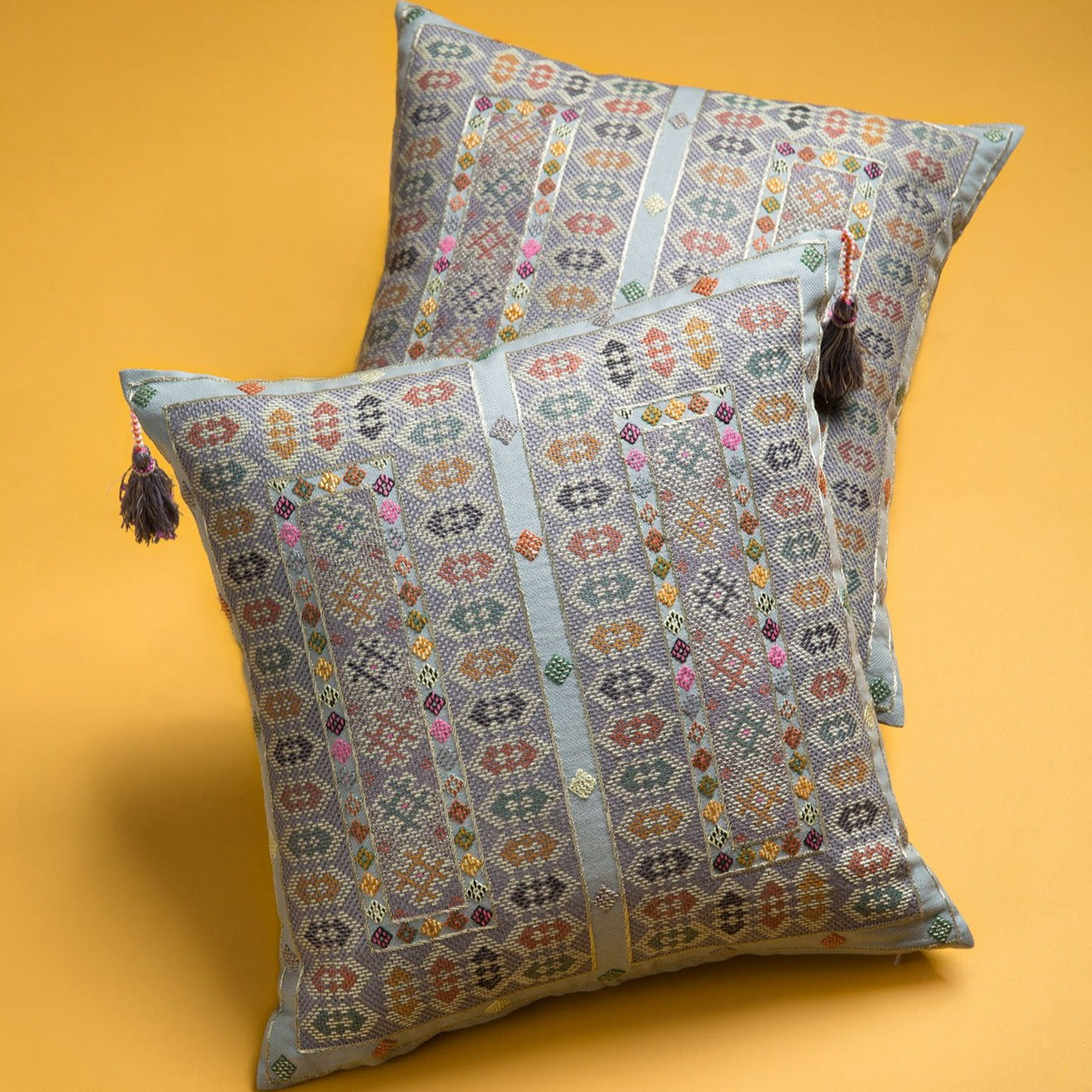 Corner detail photo of Midnight blue Zee square cushions with intense Baluchi embroidery on top of each other on a yellow background