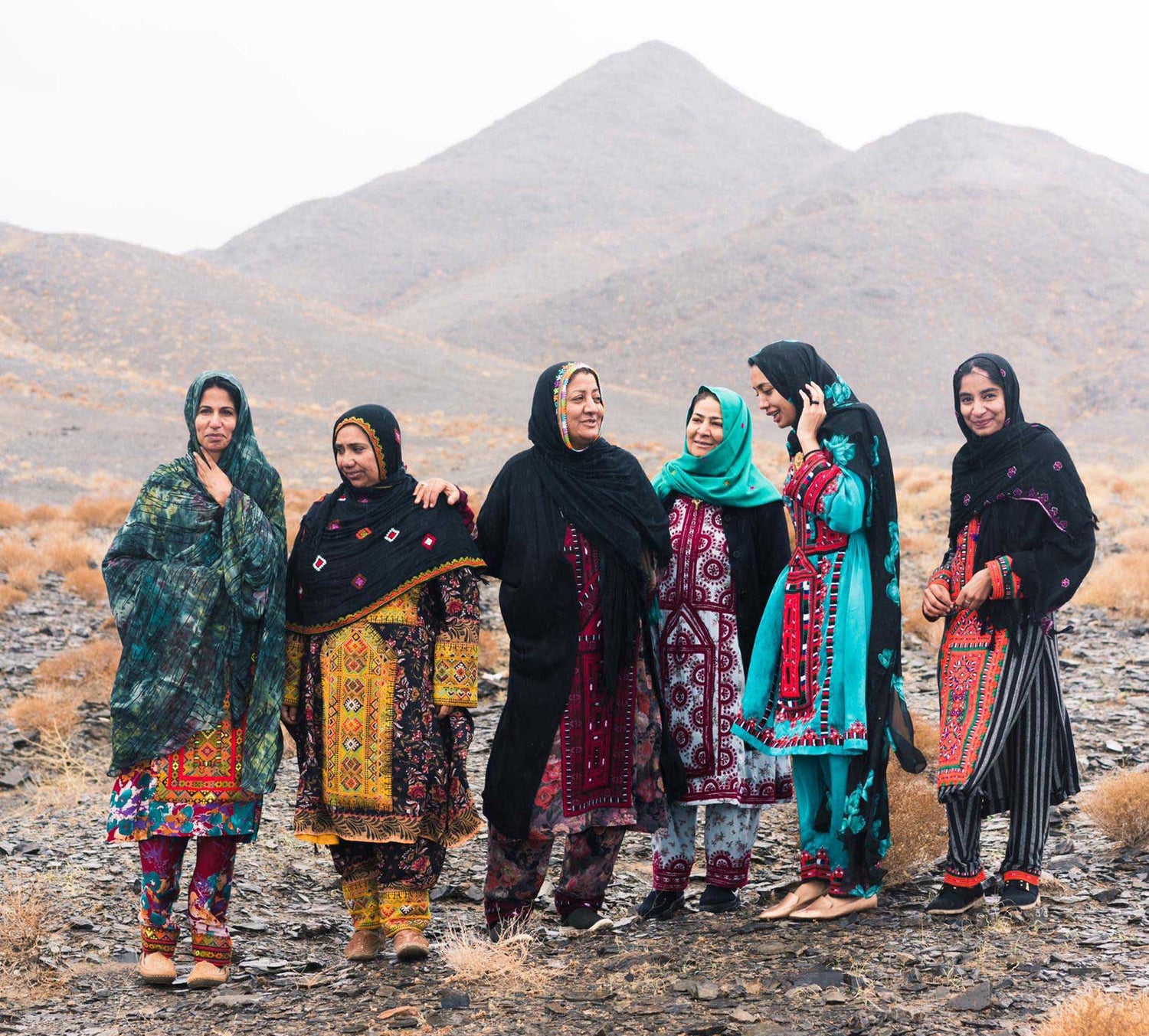 Laneh Baluchistan women embroiderers laughing in front of a mountain