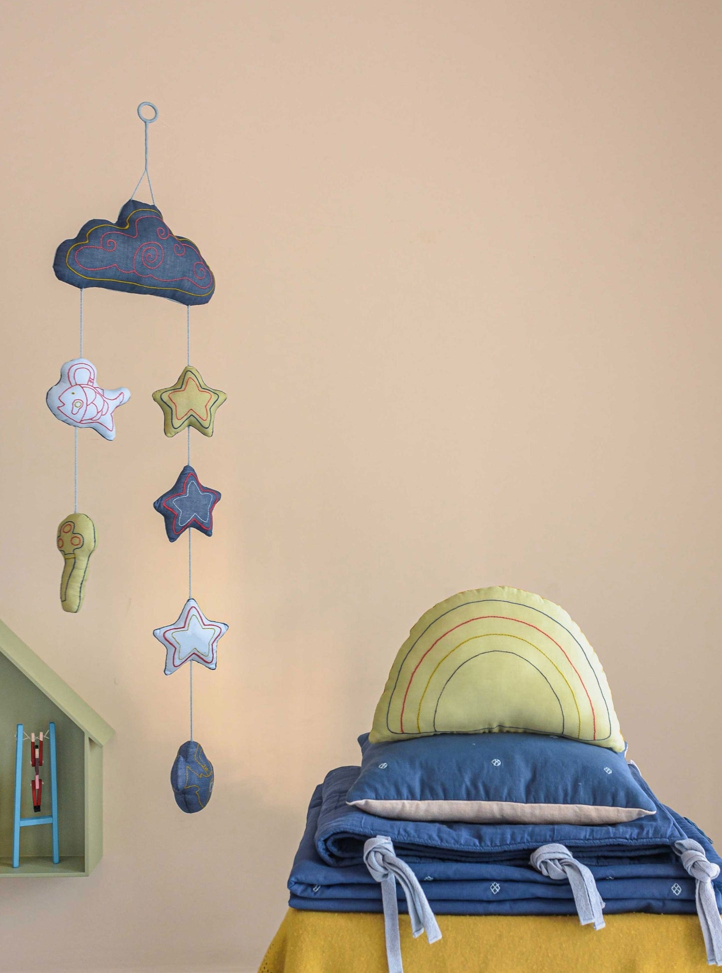 Blue bandook pillow, blanket, bumper with Lime rainbow decorative cushion stacked on top of each other while blue Moshkel gosha mobile is hanging from the ceiling 