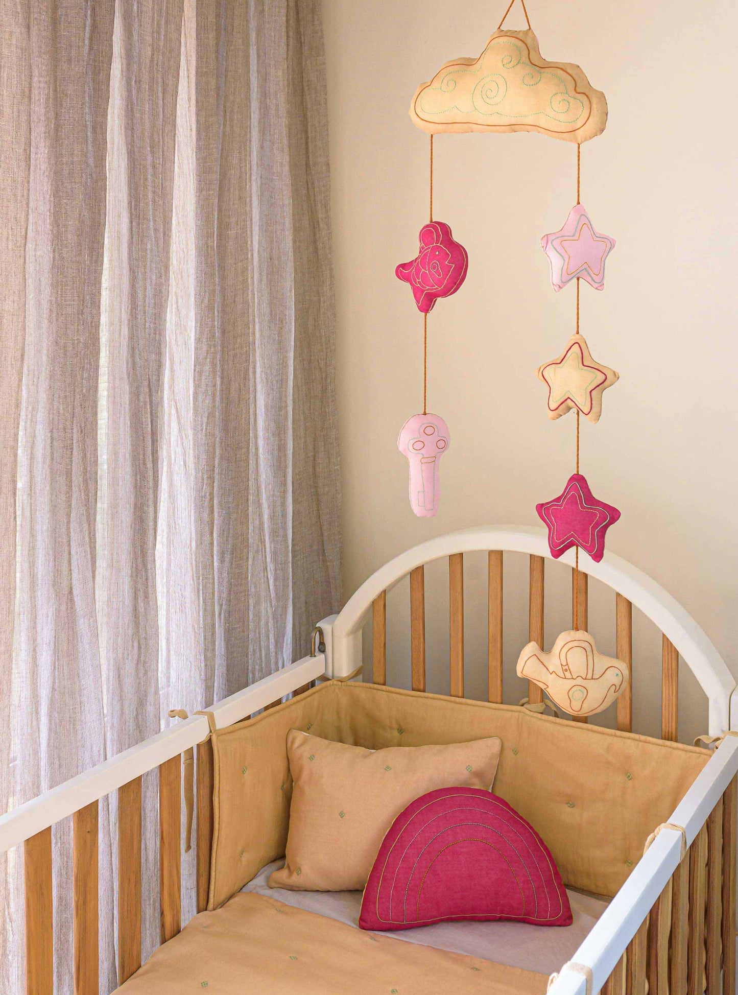 Wheat Bandook pillow, bumper, blanket and the Fuchsia Rainbow cushion and a Wheat Moshkel Gosha mobile placed in a nursery baby room