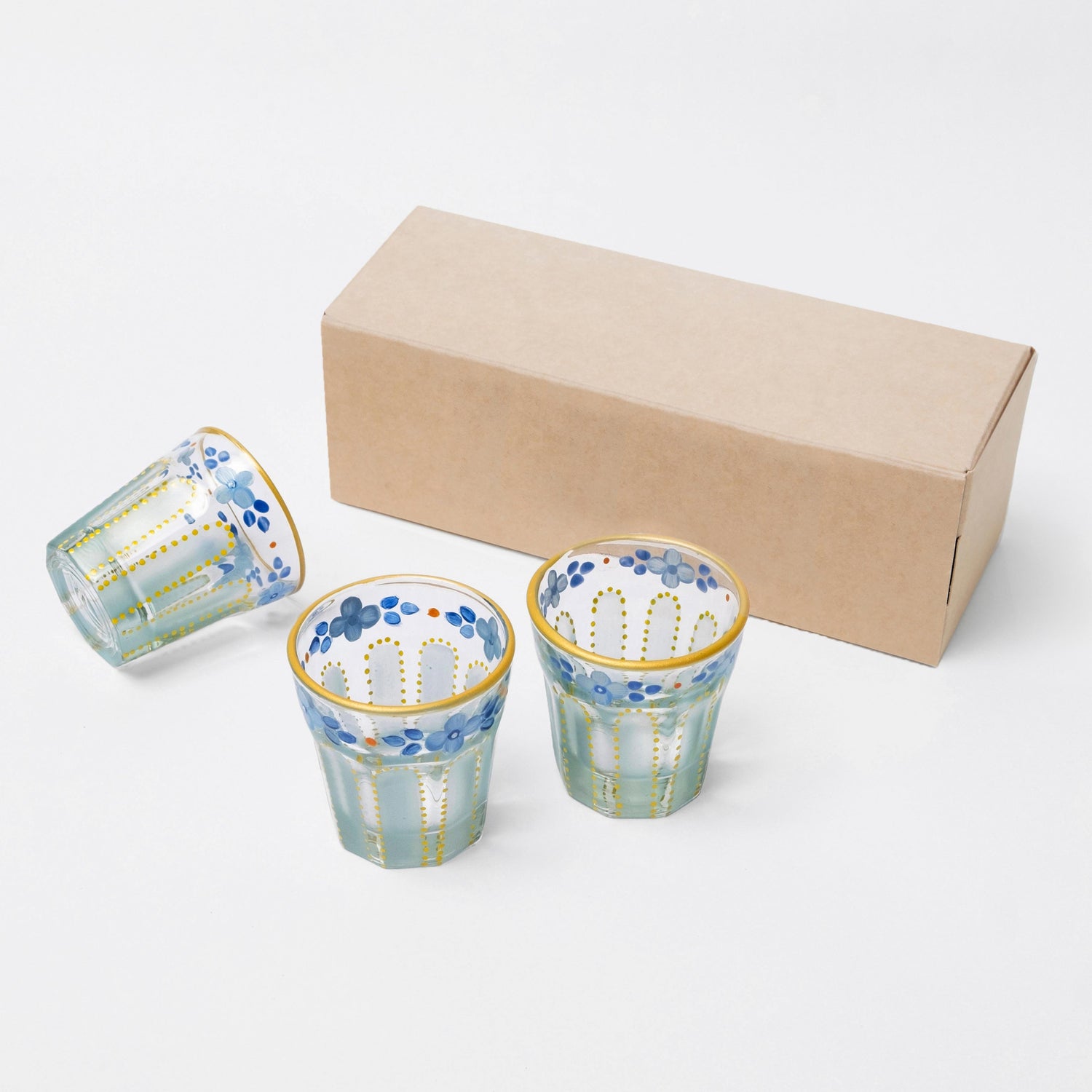 Three Nile blue shot glasses next to a kraft packaging box