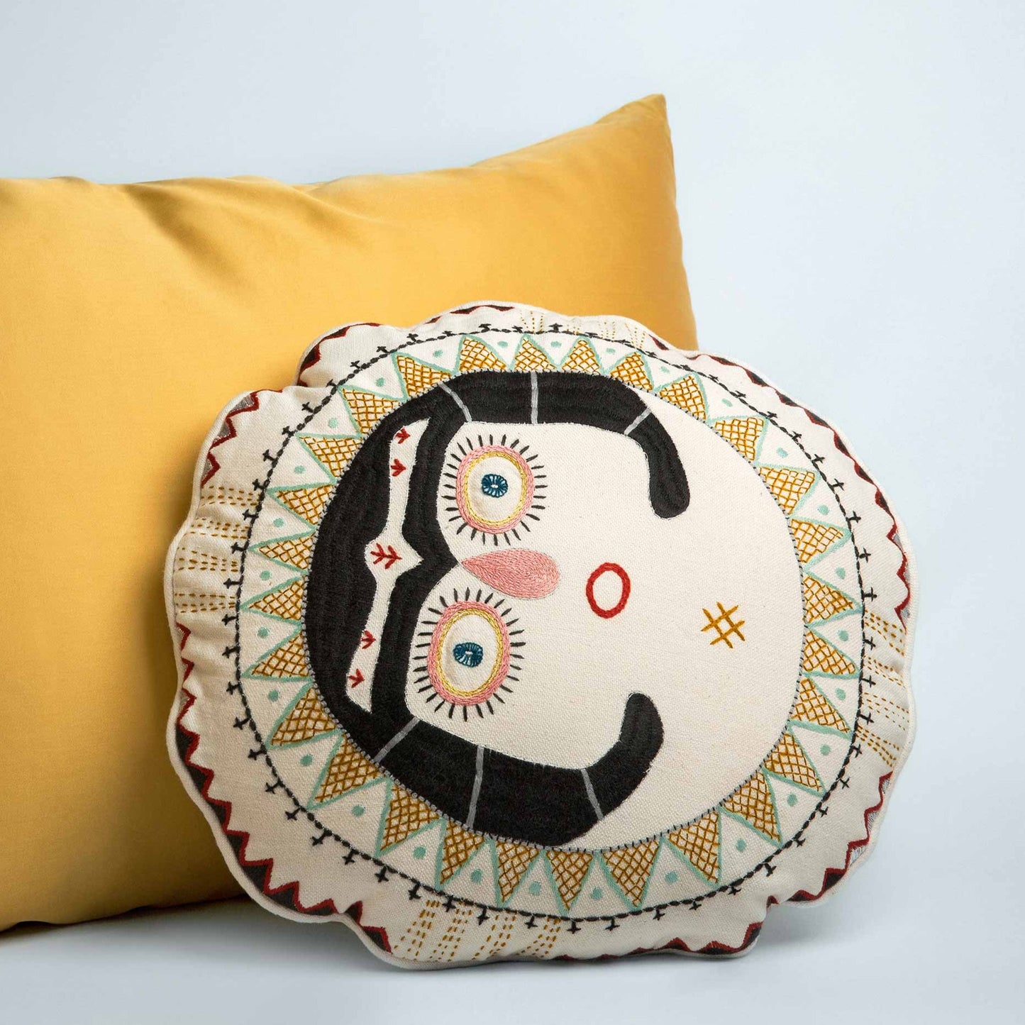 Charcoal Sun Lady cushion next to a yellow pillow